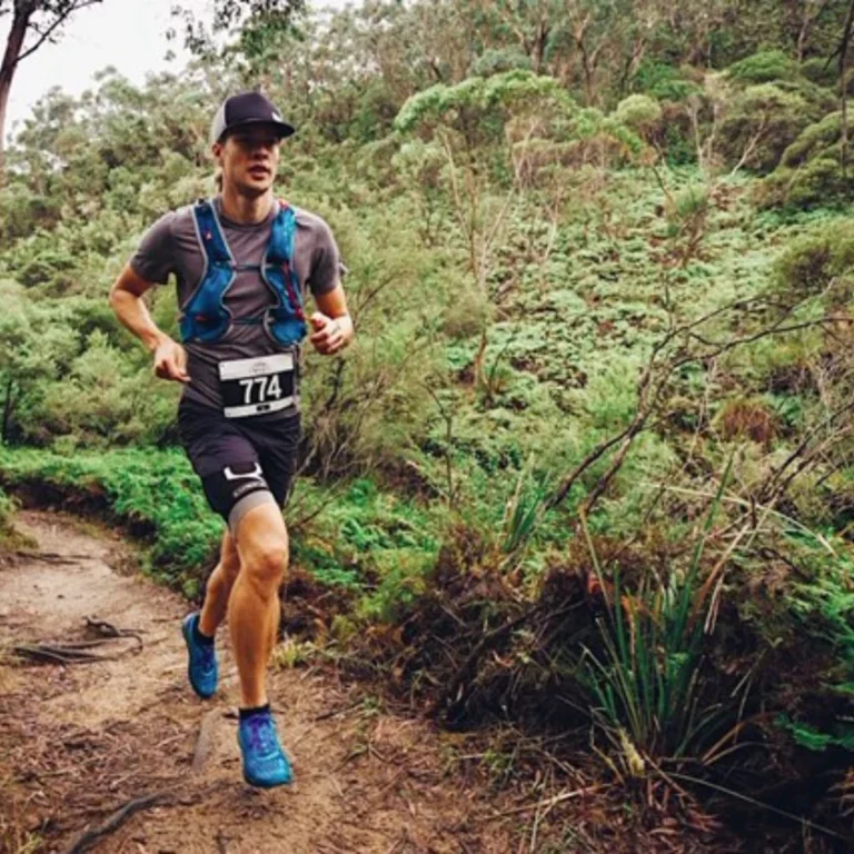 Läufer mit blauer Weste auf einem Trail im dichten Wald, voller Energie und Fokus
